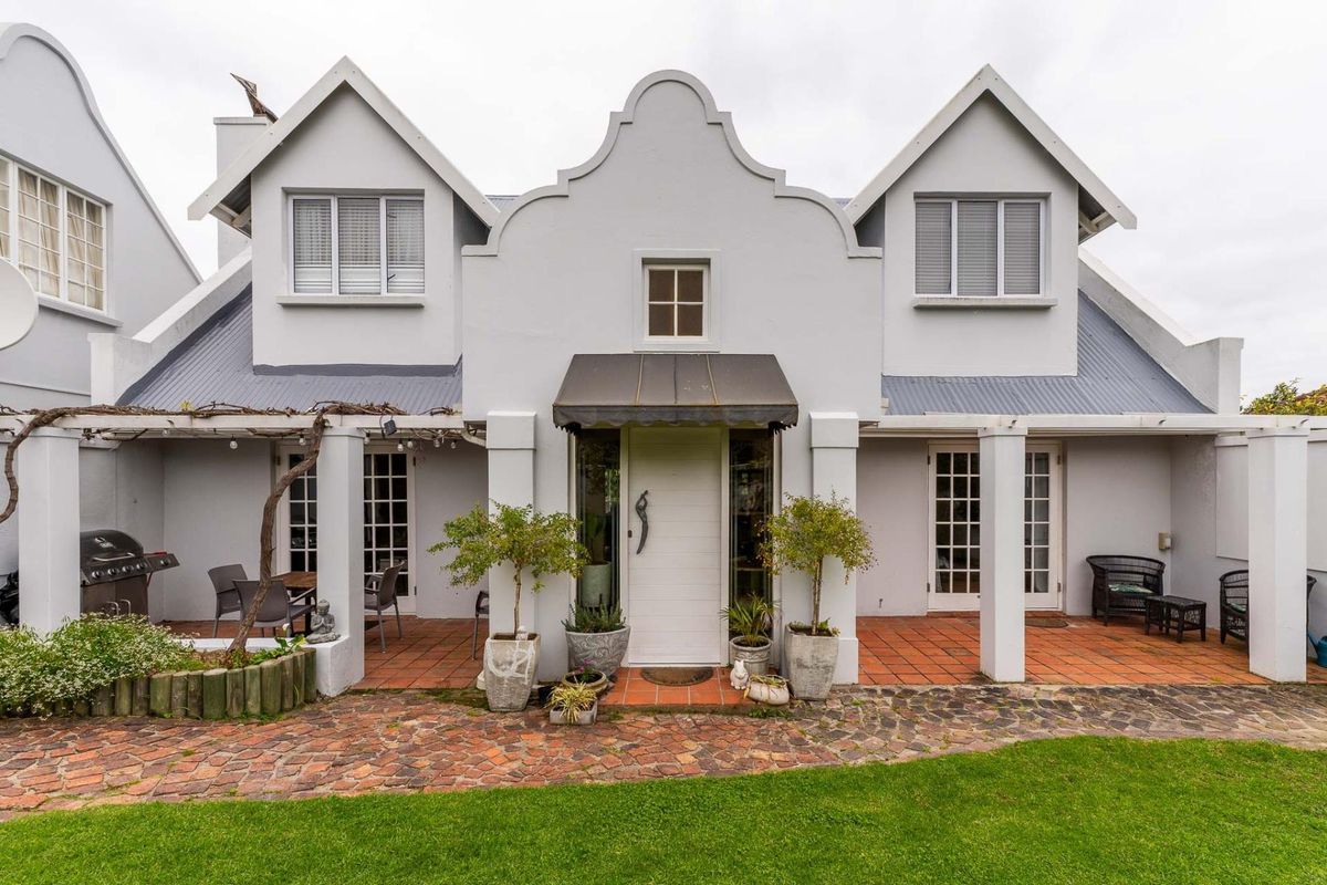 A charming rear facade featuring a gabled roofline, covered patio with terracotta tiling, and multiple sets of french doors leading into the home.