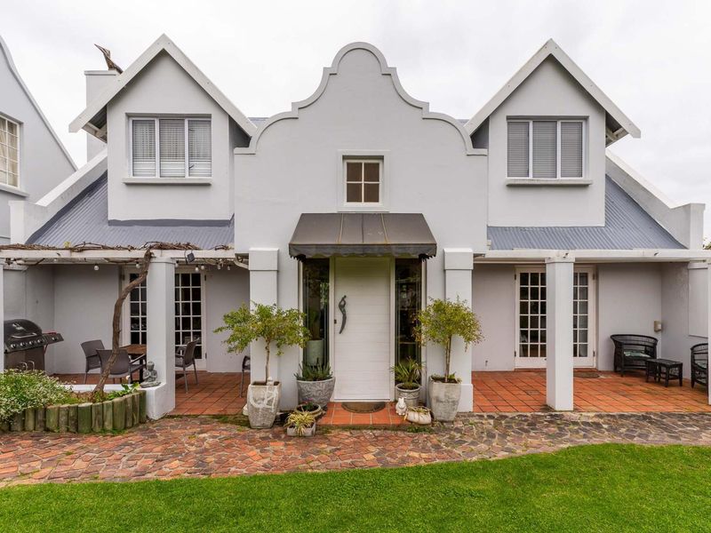 A charming rear facade featuring a gabled roofline, covered patio with terracotta tiling, and multiple sets of french doors leading into the home.