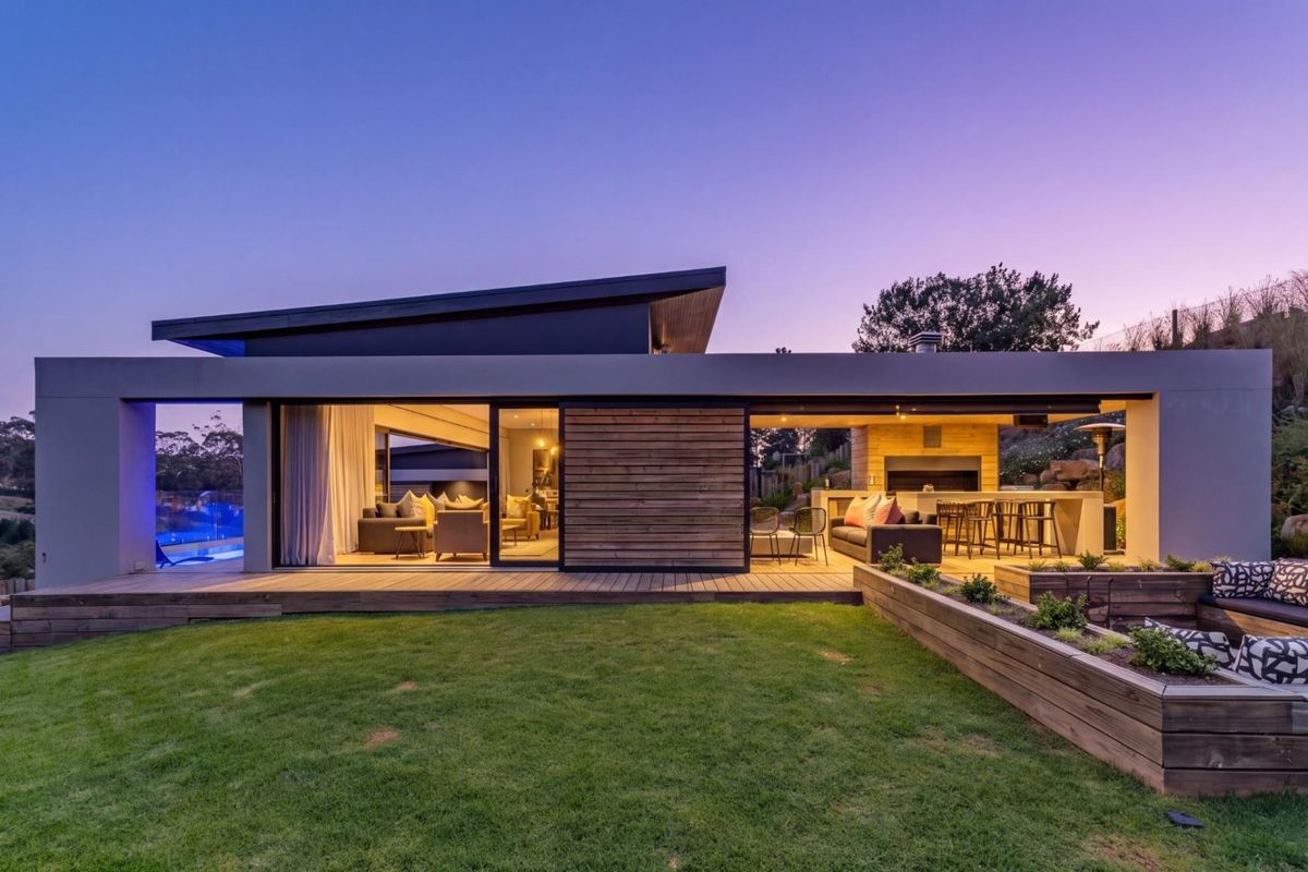 Modern rear exterior featuring timber decking, a built-in outdoor fireplace, and seamless indoor-outdoor flow through large sliding glass doors overlooking the garden and pool.