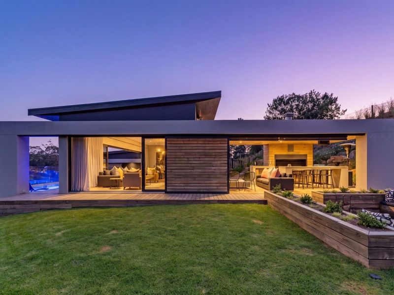 Modern rear exterior featuring timber decking, a built-in outdoor fireplace, and seamless indoor-outdoor flow through large sliding glass doors overlooking the garden and pool.