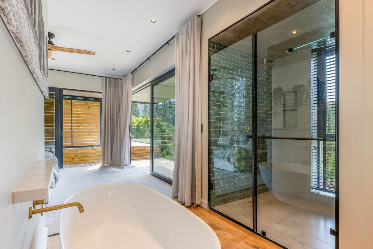 Modern bathroom featuring a sleek freestanding bathtub, a spacious walk-in shower with green subway tiles, and large sliding doors opening to a deck.