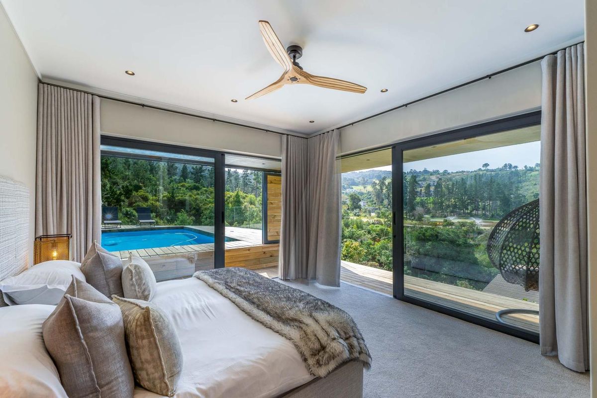 Spacious bedroom featuring large sliding glass doors with views of the pool and surrounding landscape, modern ceiling fan, and neutral carpet flooring.