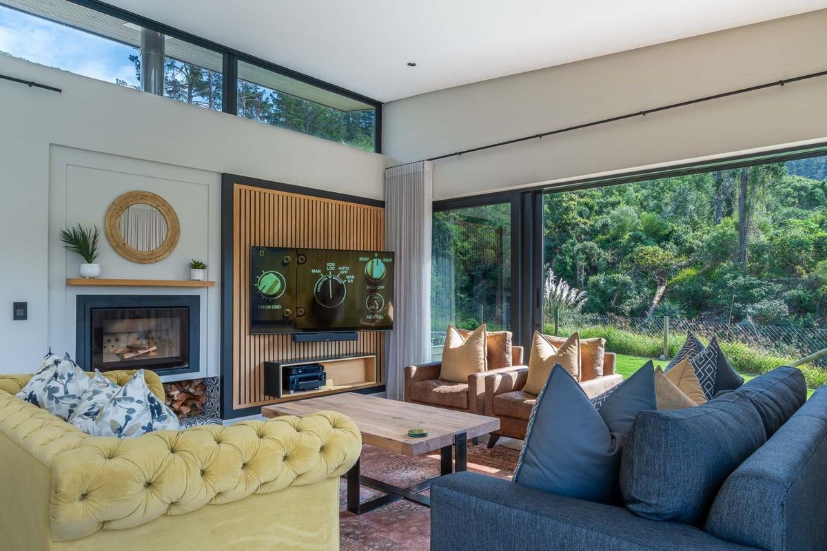 Modern living room featuring a fireplace, timber slat feature wall, clerestory windows, and large sliding glass doors opening to a lush garden view.