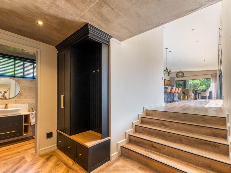 Modern entry foyer featuring custom built-in cabinetry, herringbone timber flooring, and a concrete ceiling, leading to an open-plan living area and adjacent bathroom.