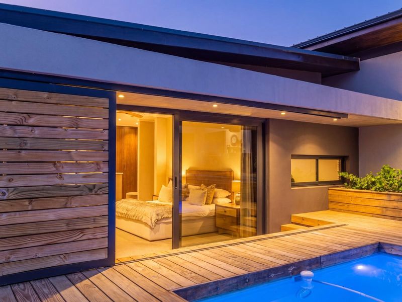 Modern outdoor pool area featuring timber decking, a built-in planter, and seamless access to the interior through large sliding glass doors.