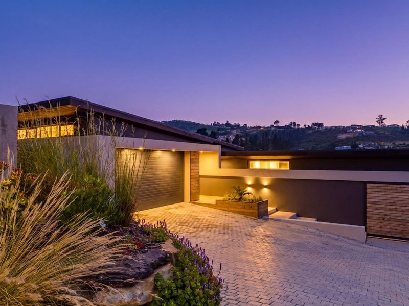 Modern architectural front facade featuring a paved driveway, automated garage, and integrated exterior lighting at dusk.