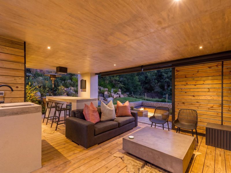A modern covered patio featuring timber decking and ceiling, a built-in concrete bar with sink, and an integrated outdoor fire pit area.