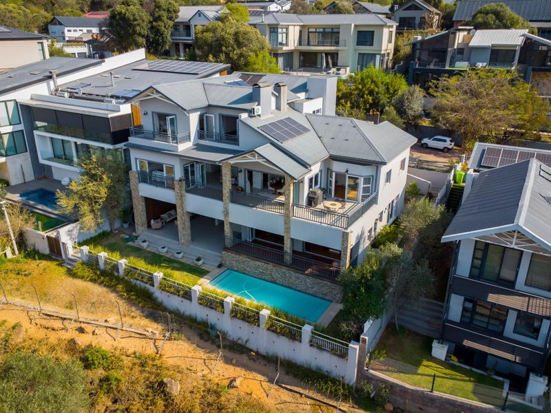 Aerial view of a multi-story residential property featuring a swimming pool, multiple balconies, solar panels, and modern stone and metal architectural finishes.