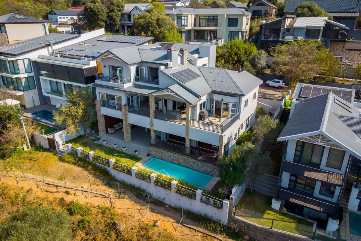 Aerial view of a multi-story residential property featuring a swimming pool, multiple balconies, solar panels, and modern stone and metal architectural finishes.