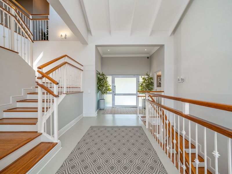 Spacious entrance hall featuring a grand timber staircase with white balustrades, vaulted ceilings, and a modern glass-panelled front door.