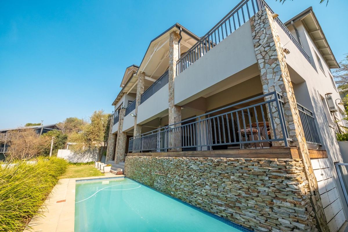 Rear elevation of a multi-story house featuring a swimming pool, stone-clad pillars, and spacious balconies with metal railings.