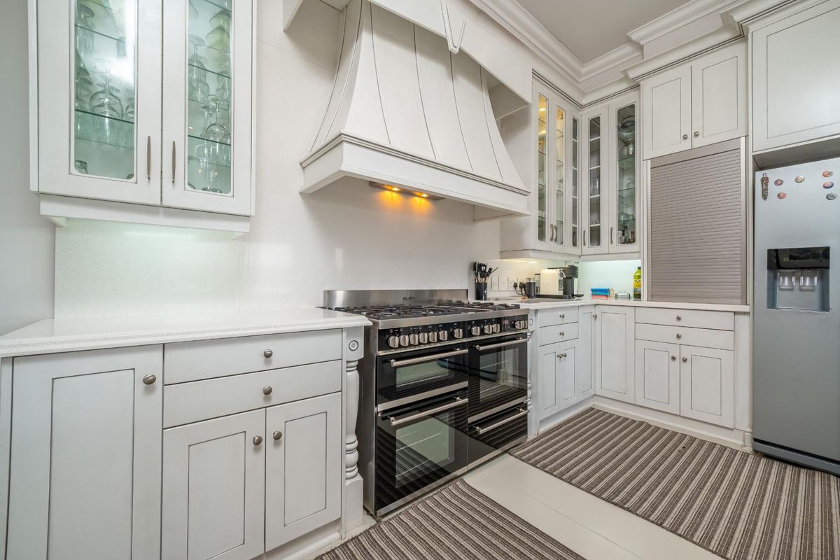 A well-appointed kitchen featuring white shaker-style cabinetry, quartz countertops, and a professional-grade gas range cooker with a custom extractor hood.