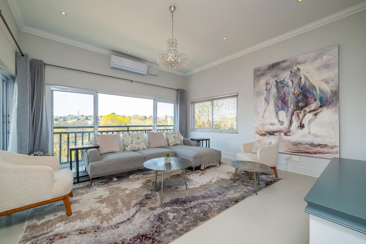 Bright and modern living room featuring large sliding glass doors with balcony access, split-system air conditioning, and elegant chandelier lighting.