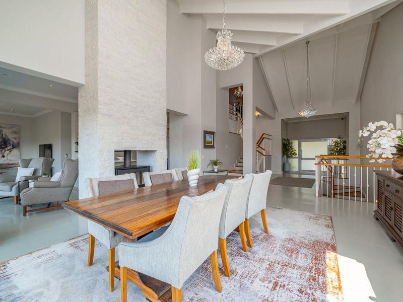 Spacious open-plan dining area featuring a striking stone fireplace, vaulted ceilings with exposed beams, and an elegant staircase leading to the upper level.