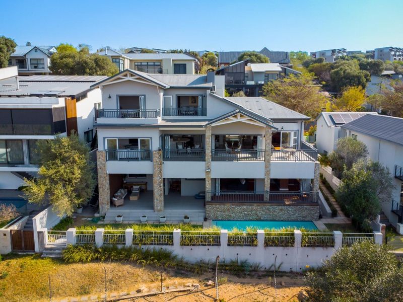 Aerial view of a multi-story residential property featuring a swimming pool, stone-clad pillars, and multiple balconies with sliding door access.
