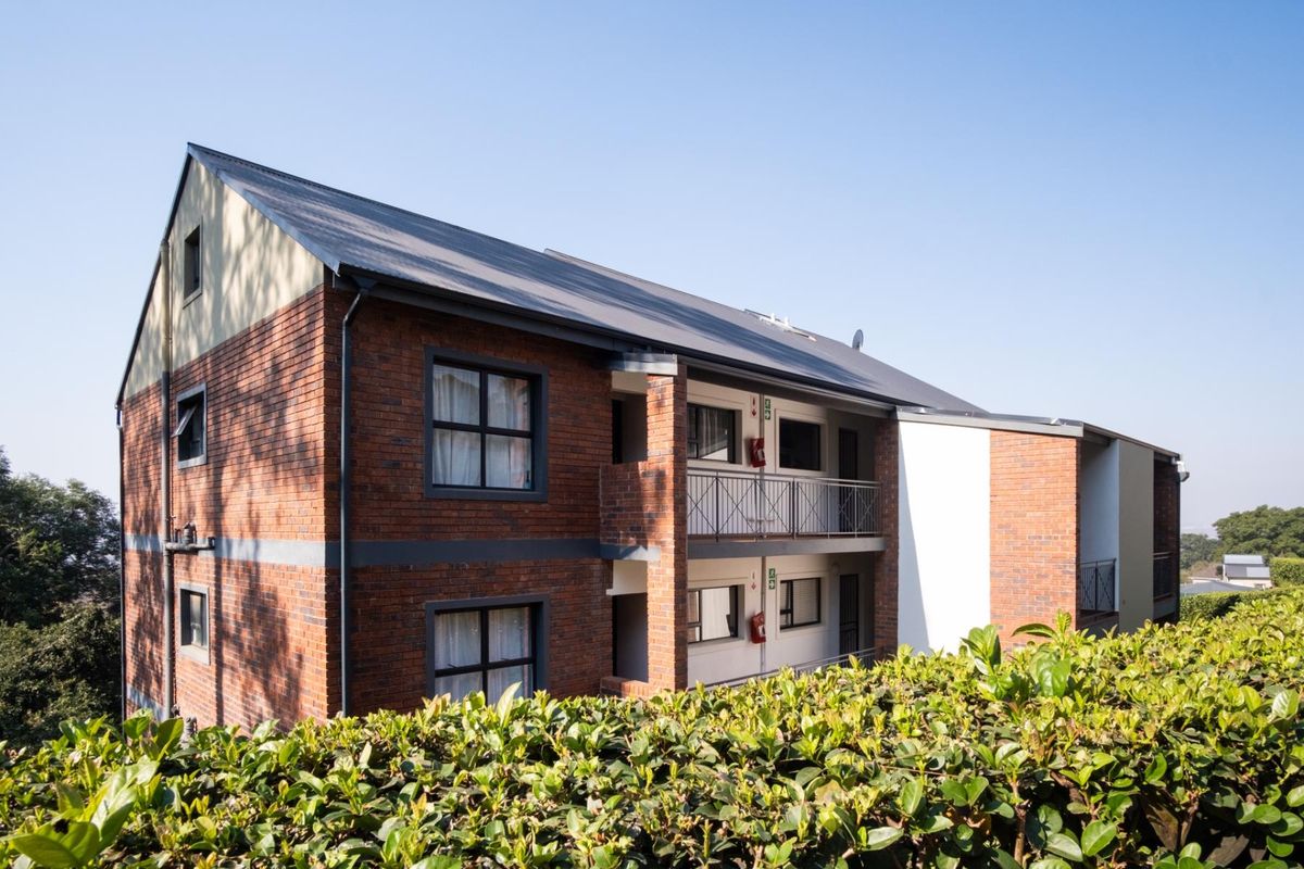 A view of the rear elevation of a multi-story apartment building featuring face brick construction, pitched metal roofing, and private balconies with metal railings.