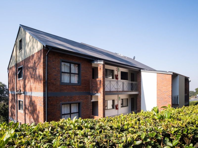 A view of the rear elevation of a multi-story apartment building featuring face brick construction, pitched metal roofing, and private balconies with metal railings.