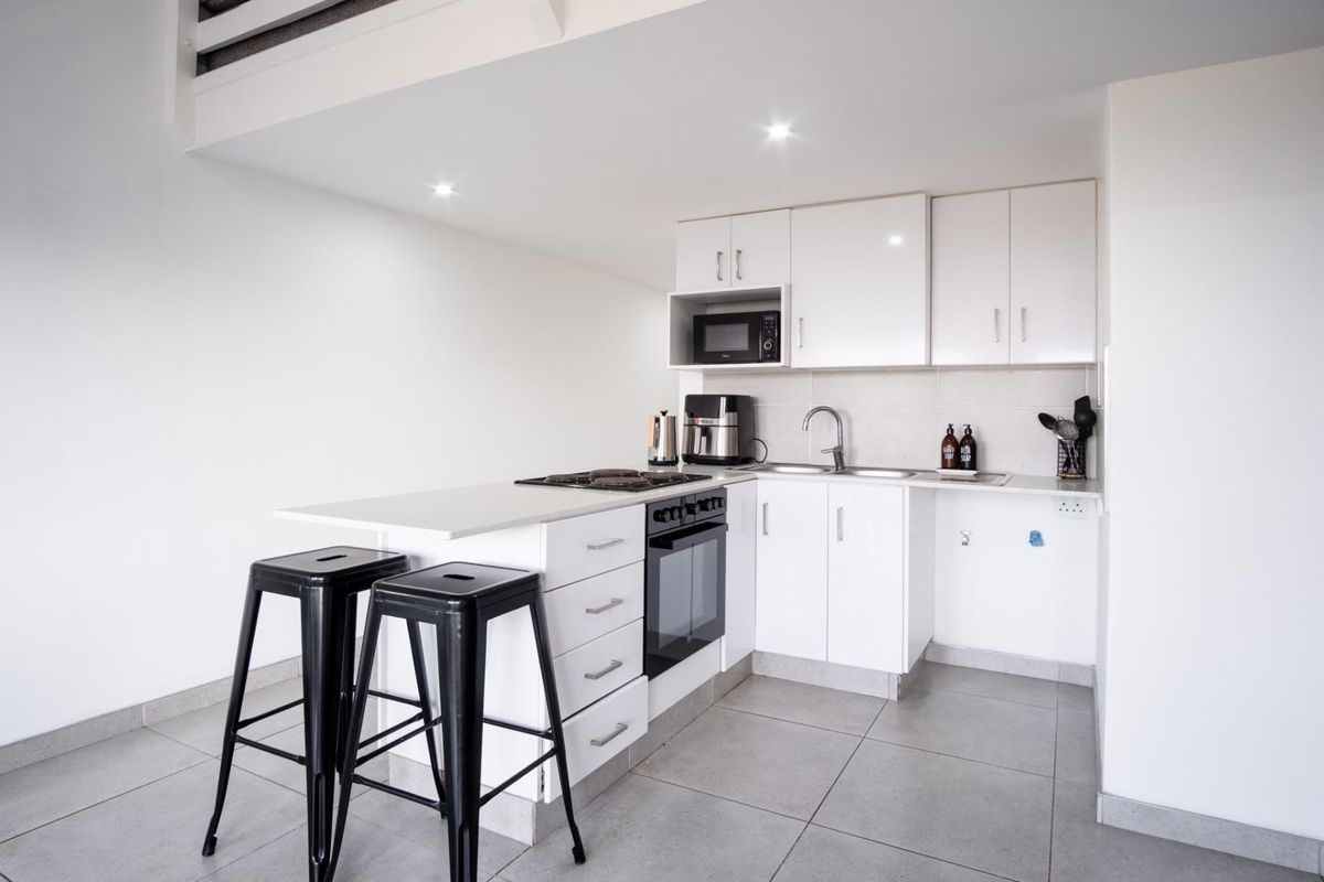 Compact modern kitchen featuring white cabinetry, built-in oven, hob, microwave, and tiled flooring, providing a functional and clean culinary space.