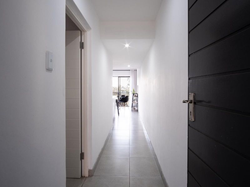 A clean, well-lit hallway featuring neutral tiled flooring and modern recessed downlighting, providing a seamless transition between the apartment's living spaces.
