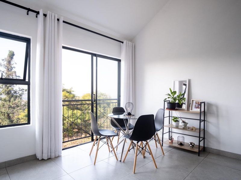 Bright living area featuring large sliding glass doors with access to a balcony, neutral tiled flooring, and modern black window frames.
