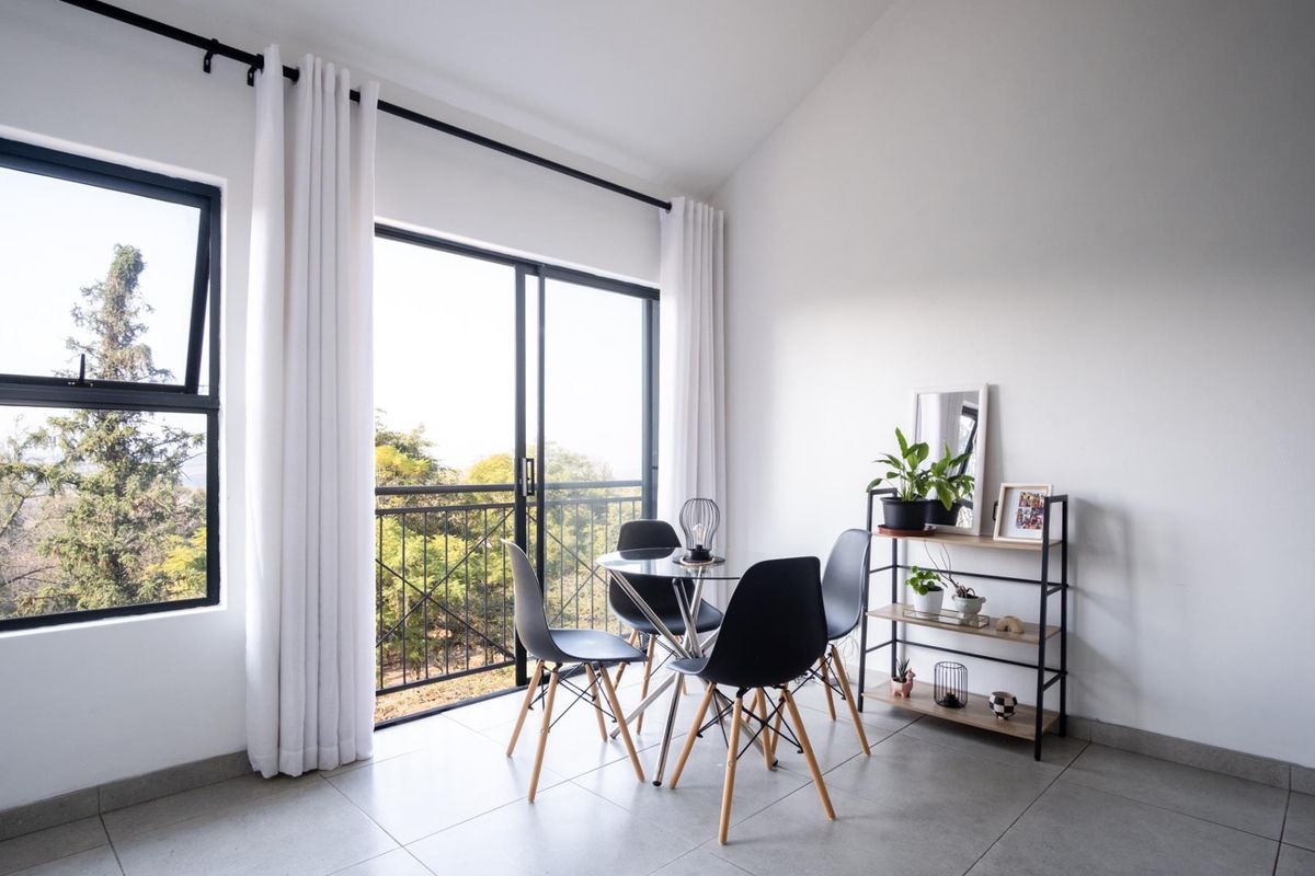 Bright living area featuring large sliding glass doors with access to a balcony, neutral tiled flooring, and modern black window frames.