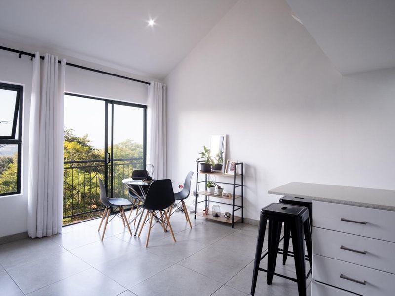 Modern open-plan living area featuring tiled floors, a vaulted ceiling, and a sliding glass door leading to a balcony with scenic views.