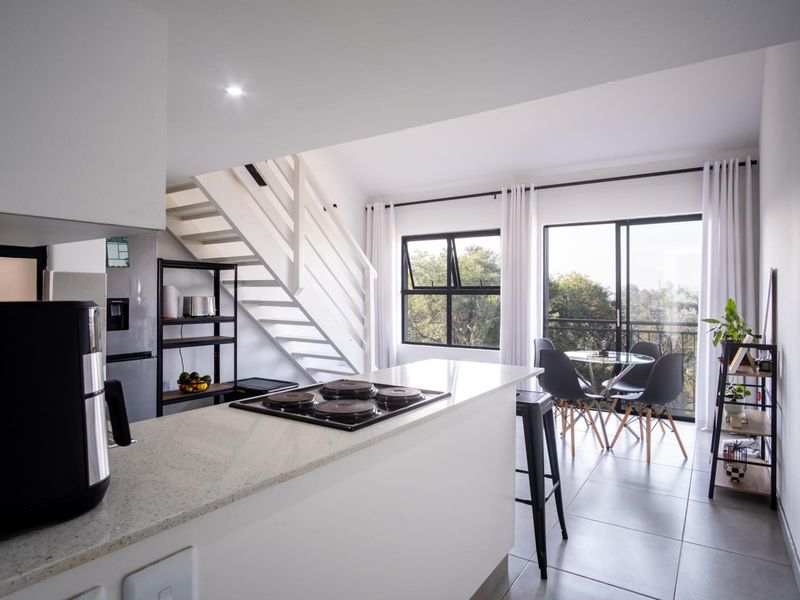 Modern open-plan living area featuring a kitchen island with an integrated hob, a staircase, and sliding doors leading to a balcony with scenic views.