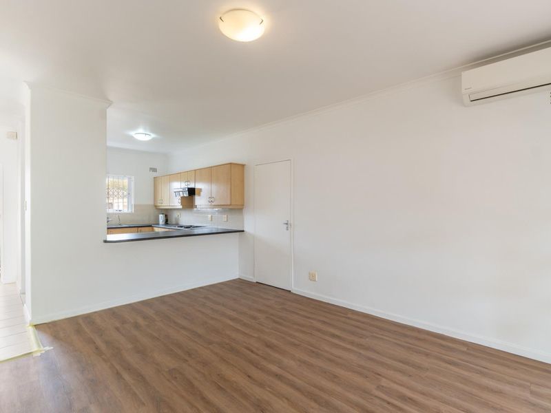 An open-plan living area featuring laminate flooring, a split-system air conditioner, and a functional kitchen with wood-finish cabinetry and a breakfast bar.