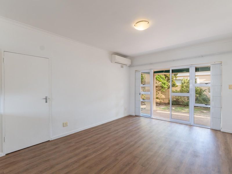 Bright and spacious living room featuring modern laminate flooring, a split-system air conditioner, and large sliding glass doors providing access to the outdoor area.