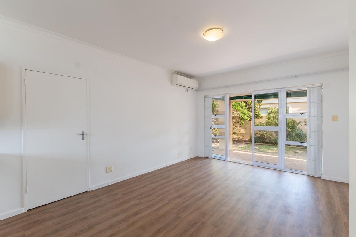 Bright and spacious living room featuring modern laminate flooring, a split-system air conditioner, and large sliding glass doors providing access to the outdoor area.