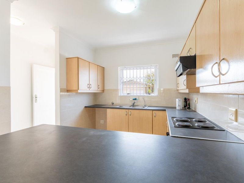 A functional kitchen featuring light wood-finish cabinetry, dark laminate countertops, a built-in electric hob, and a tiled splashback.