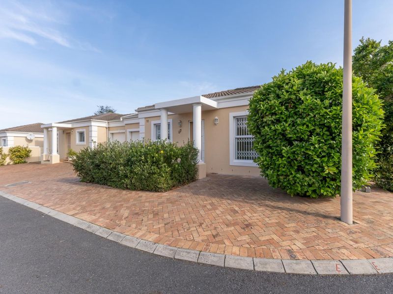 Front elevation of a well-maintained townhouse featuring a brick-paved driveway, covered entrance porch with columns, and established garden landscaping.