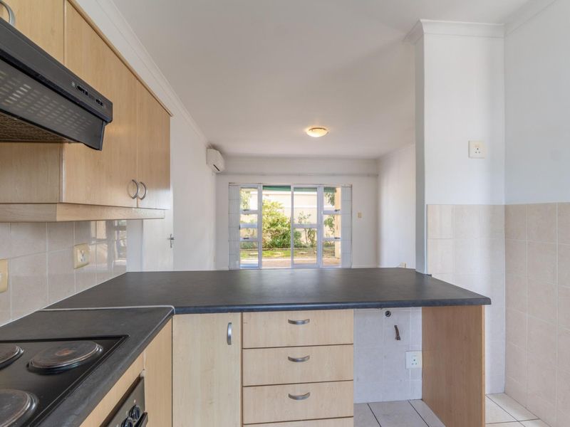 A functional kitchen featuring light wood cabinetry, dark countertops, and an integrated hob, flowing into an open-plan living area with garden access.