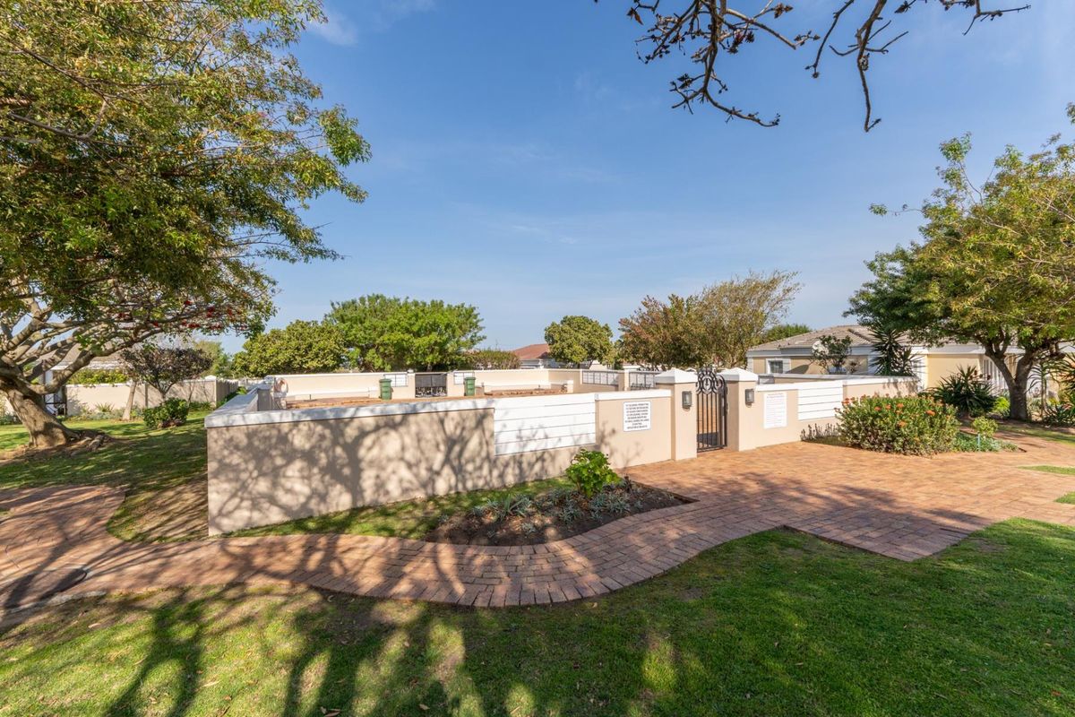 A well-maintained outdoor area featuring a brick paved pathway, perimeter wall with a metal gate, and established garden landscaping.