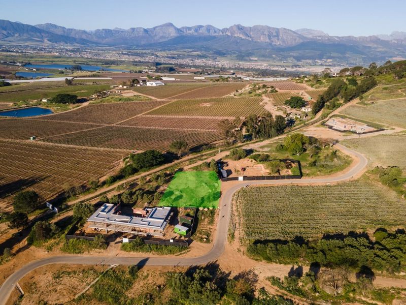 Aerial view of a vacant residential plot situated within a scenic agricultural estate, featuring established road access and mountain views.