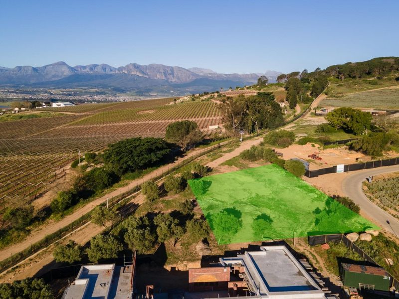 An aerial view of a vacant residential plot situated in a scenic landscape with mountain views and surrounding vineyards.