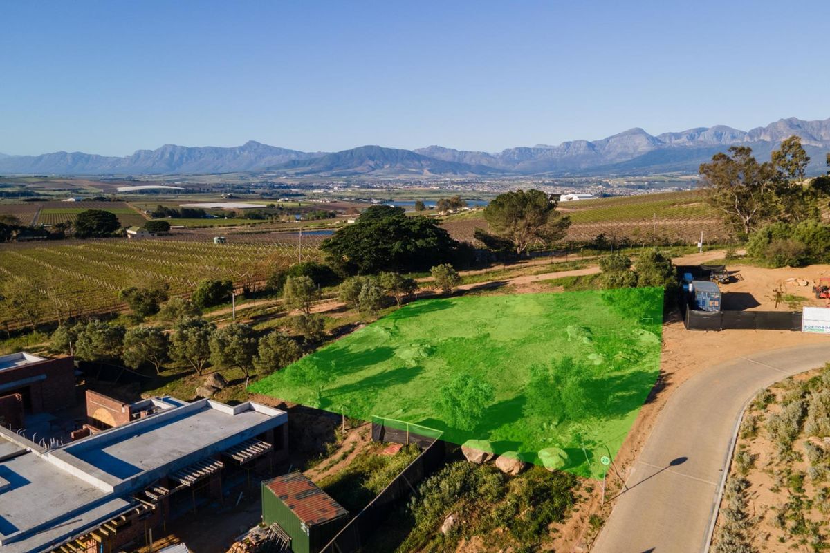 Aerial view of a vacant residential plot with mountain views, featuring road access and surrounding agricultural landscape.