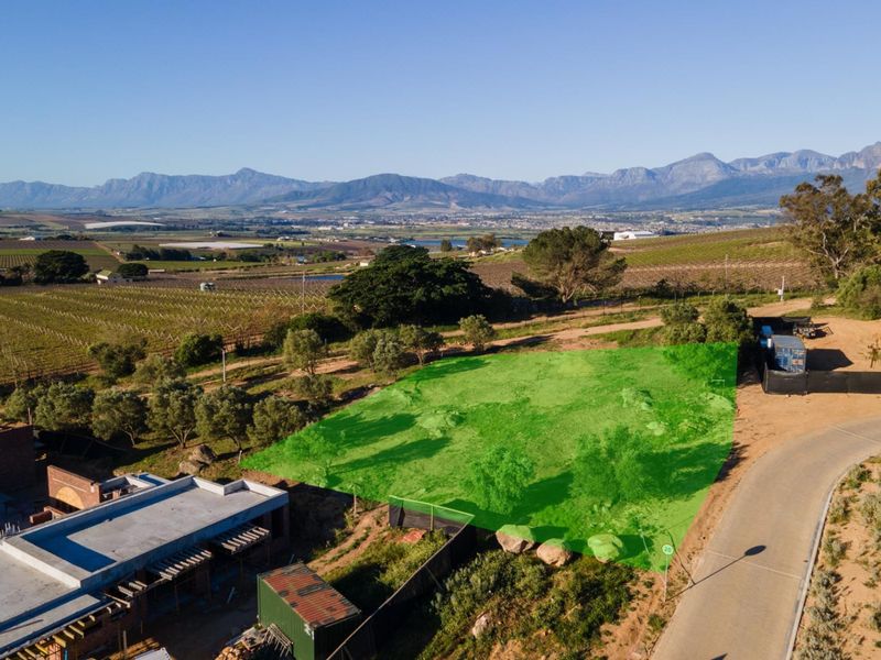Aerial view of a vacant residential plot with mountain views, featuring road access and surrounding agricultural landscape.