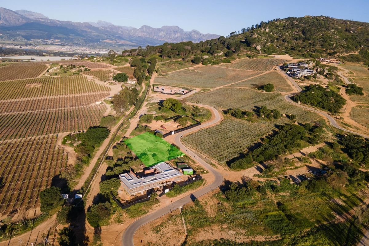 Aerial view of a residential land plot highlighted in green, situated within a scenic rural estate with mountain views and surrounding vineyards.