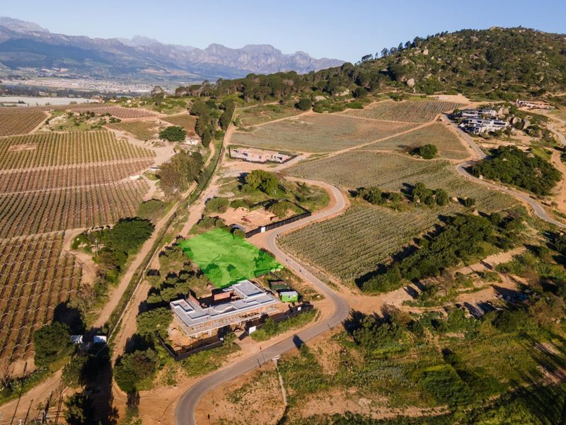 Aerial view of a residential land plot highlighted in green, situated within a scenic rural estate with mountain views and surrounding vineyards.
