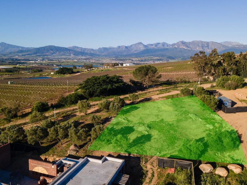 An aerial view of a vacant residential plot with scenic mountain and vineyard views in the surrounding area.