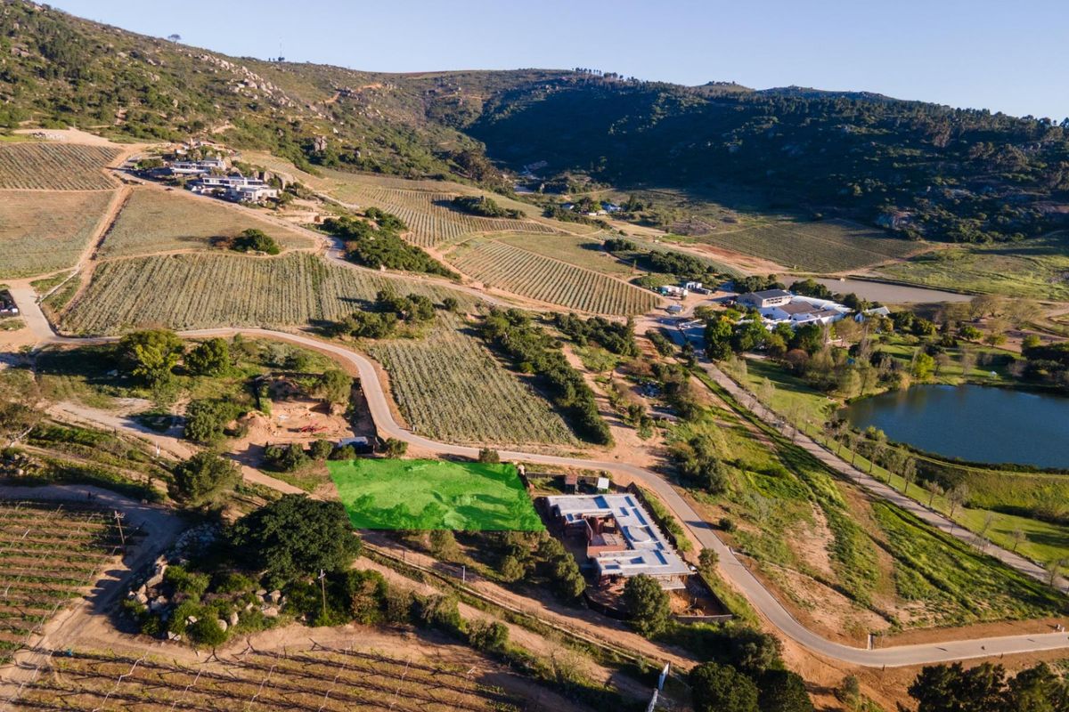 Aerial view of a vacant residential land plot situated within a scenic agricultural estate, featuring established access roads and surrounding natural landscape.