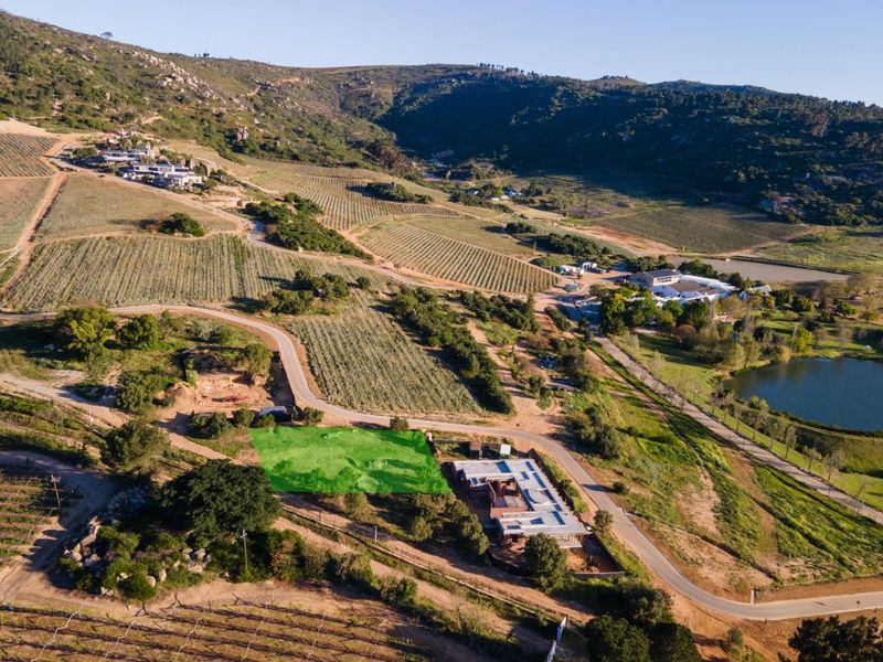 Aerial view of a vacant residential land plot situated within a scenic agricultural estate, featuring established access roads and surrounding natural landscape.