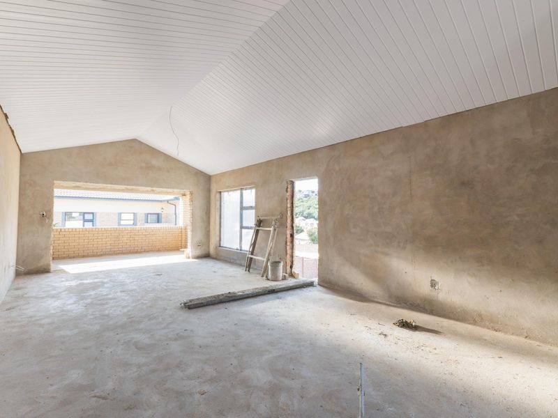 An unfinished living room space featuring a high vaulted ceiling with white paneling, concrete flooring, and open access to an outdoor patio area.