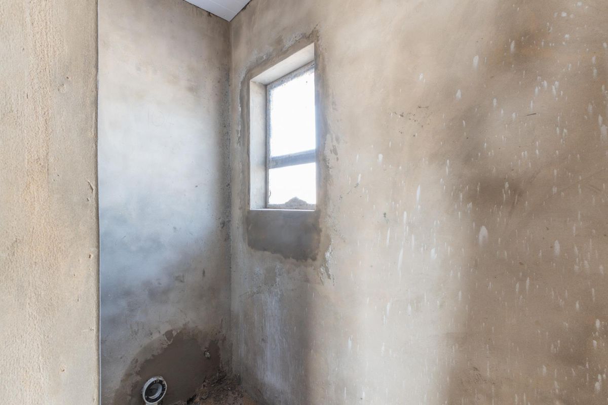 An unfinished bathroom space featuring raw plaster walls and a plumbing outlet, ready for final finishes and fixtures.