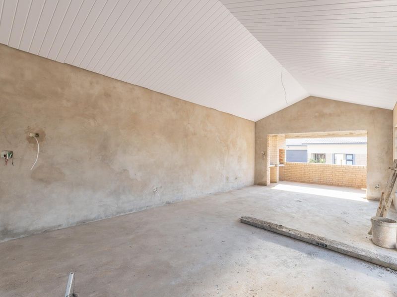 An unfinished open-plan living area featuring a vaulted ceiling, exposed plaster walls, and concrete flooring, leading out to a covered patio space.