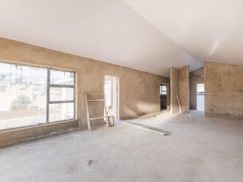 An unfinished open-plan living area featuring exposed plaster walls, concrete flooring, and a white tongue and groove ceiling, currently in a shell state.