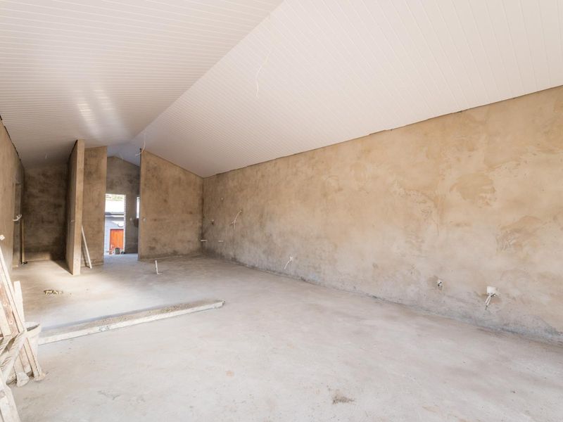 An unfinished interior space featuring vaulted ceilings, exposed plaster walls, and concrete flooring, currently in a shell condition awaiting final finishes.