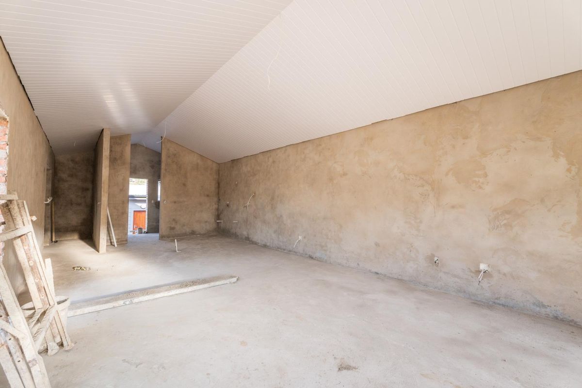 An unfinished interior space featuring vaulted ceilings, exposed plaster walls, and concrete flooring, currently in a shell condition awaiting final finishes.