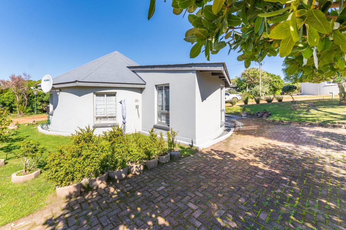 Rear view of the property featuring a brick paved driveway, landscaped garden area, and a well-maintained exterior facade with a tiled roof.